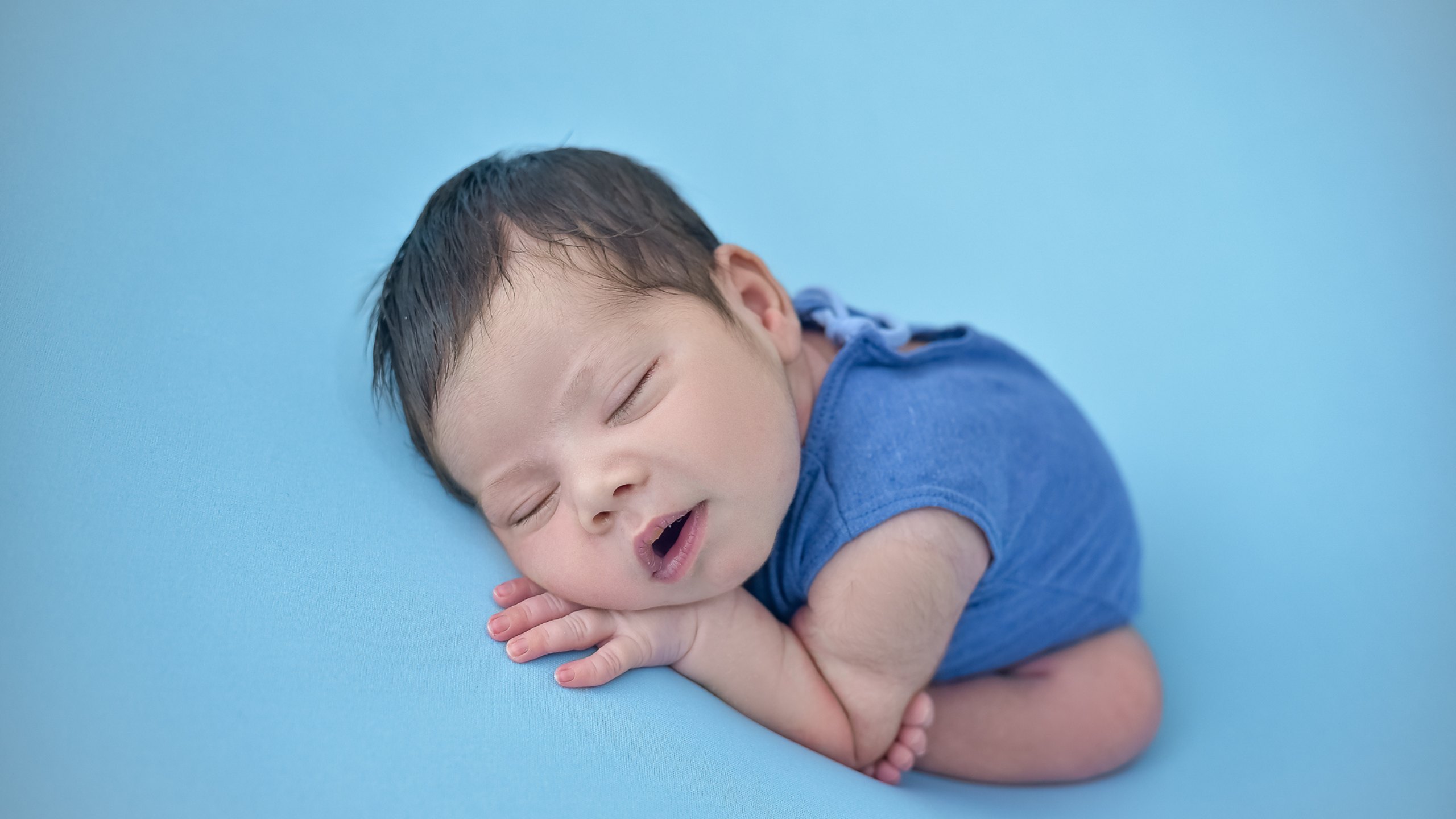 Bebê recém-nascido dormindo em fundo azul, com pele limpa após tratamento da acne neonatal