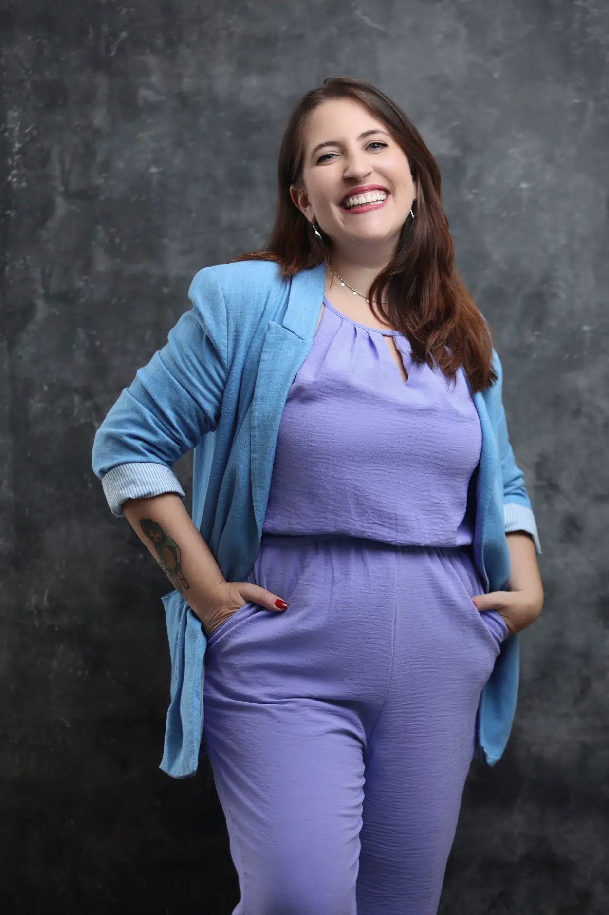 Carla toscano sorrindo, vestindo blazer azul e macacão lilás, em um fundo texturizado