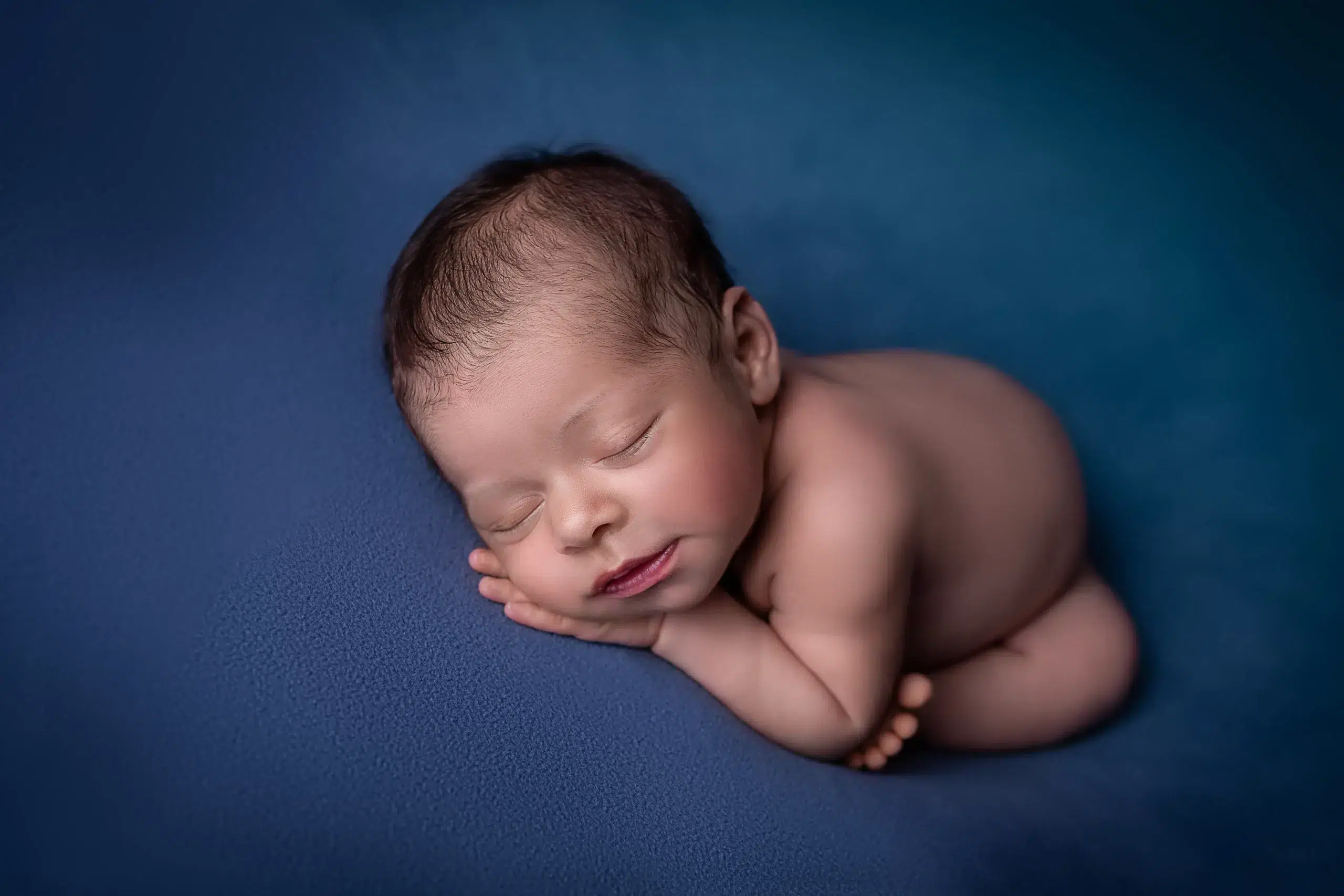 Bebê recém-nascido dormindo sobre fundo azul em ensaio newborn, pós-produção