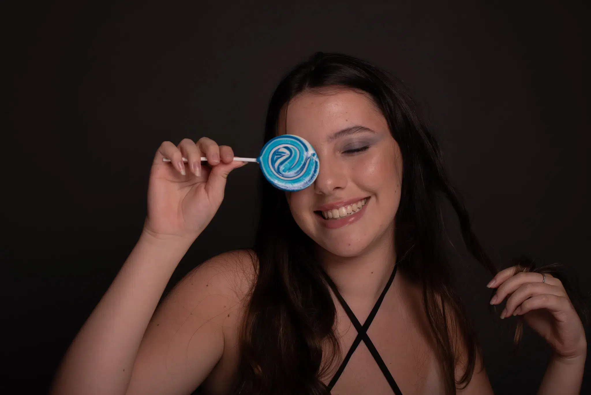 Modelo sorrindo e segurando pirulito azul, antes da pós-produção